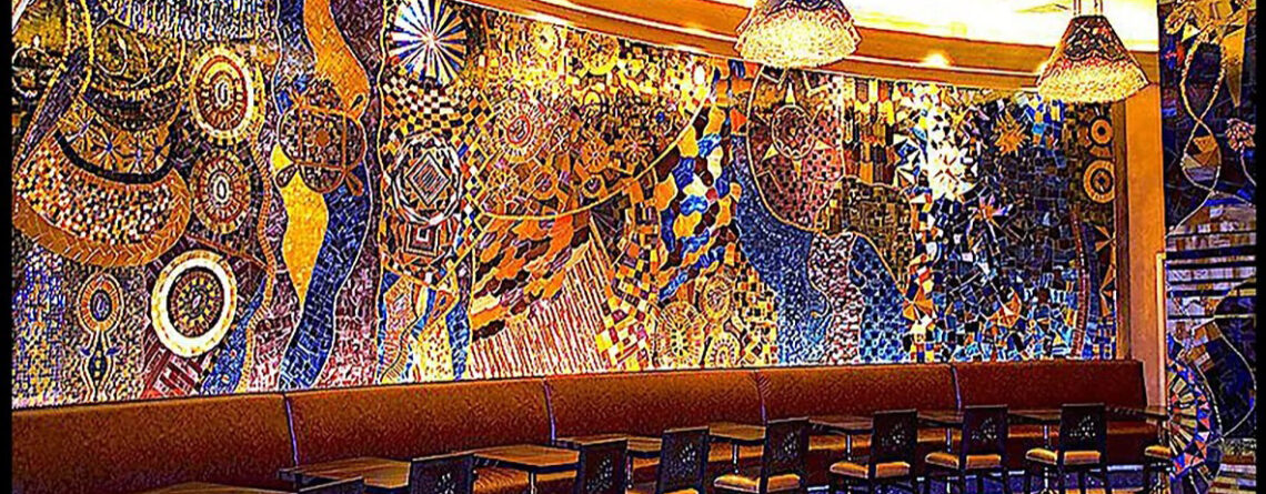 Large handcrafted stained glass and mirror mosaic feature wall by Allison Eden Studios at Mohegan Sun Casino featuring vibrant abstract patterns in blue, gold, bronze, and iridescent glass.