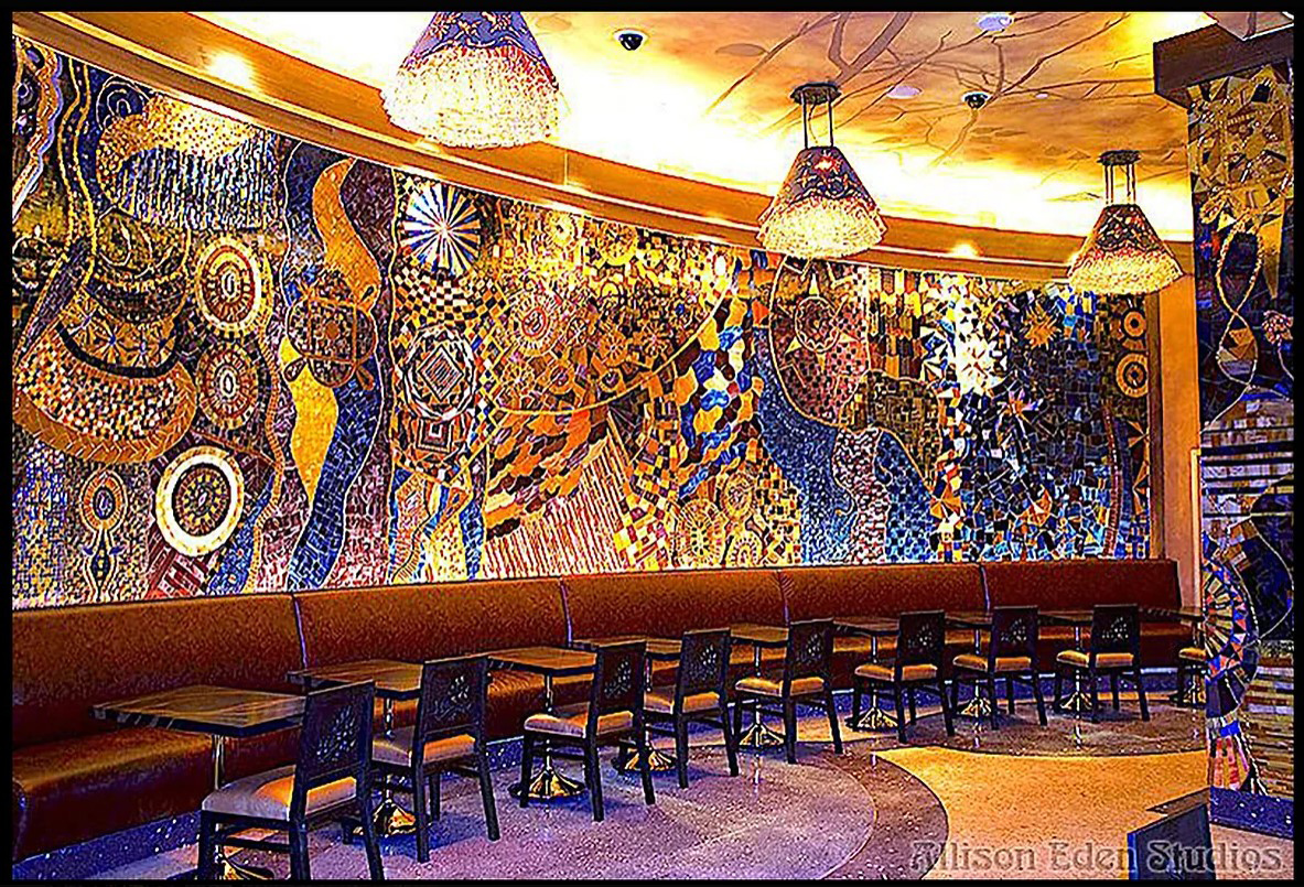 Large handcrafted stained glass and mirror mosaic feature wall by Allison Eden Studios at Mohegan Sun Casino featuring vibrant abstract patterns in blue, gold, bronze, and iridescent glass.