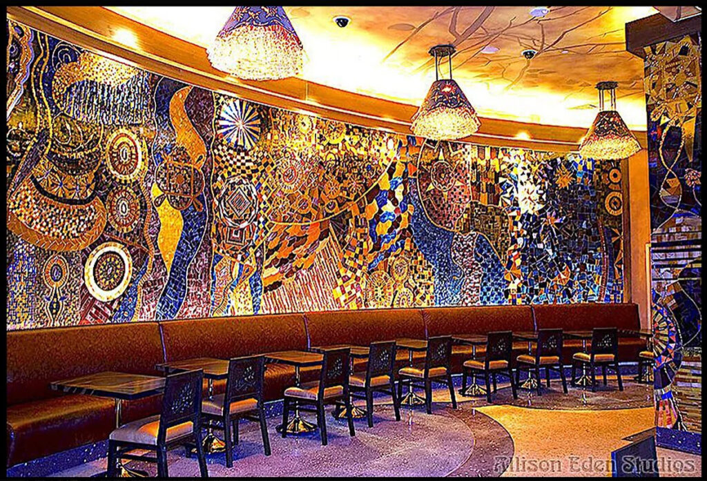Large handcrafted stained glass and mirror mosaic feature wall by Allison Eden Studios at Mohegan Sun Casino featuring vibrant abstract patterns in blue, gold, bronze, and iridescent glass.