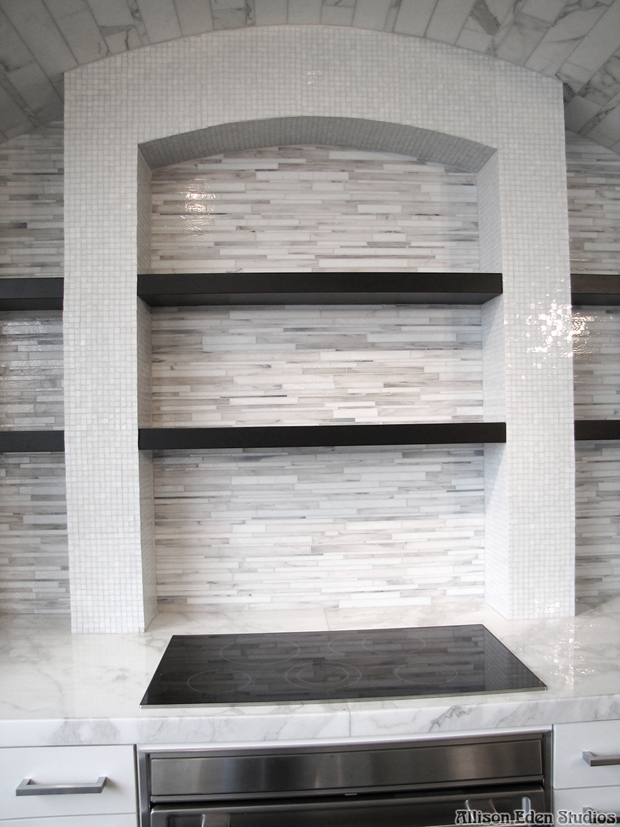 Luxury white and gray custom linear glass mosaic Barcode™ kitchen backsplash by Allison Eden Studios featuring handcrafted stained glass that complements Calacatta marble countertops, walls, and flooring in a contemporary designer kitchen with shelves.