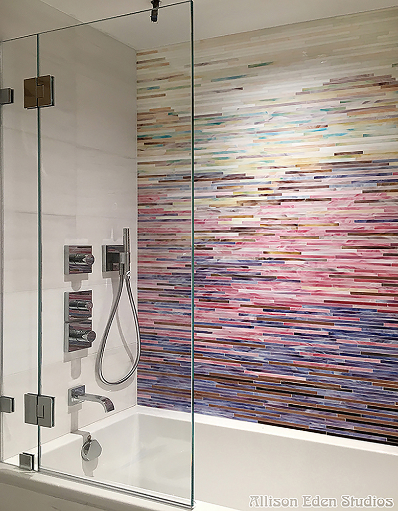 Custom stained glass mosaic shower wall featuring a handcrafted linear gradient in white, pink, blue, bronze, and aqua tones by Allison Eden Studios, paired with white porcelain tile for a luxurious spa-inspired bathroom.