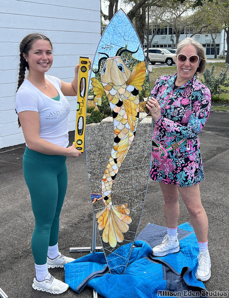 Koi Fish Surfboard at ASD Surfaces with glass mosaic artist Allison Eden setting up piece for show at The Colony Hotel.