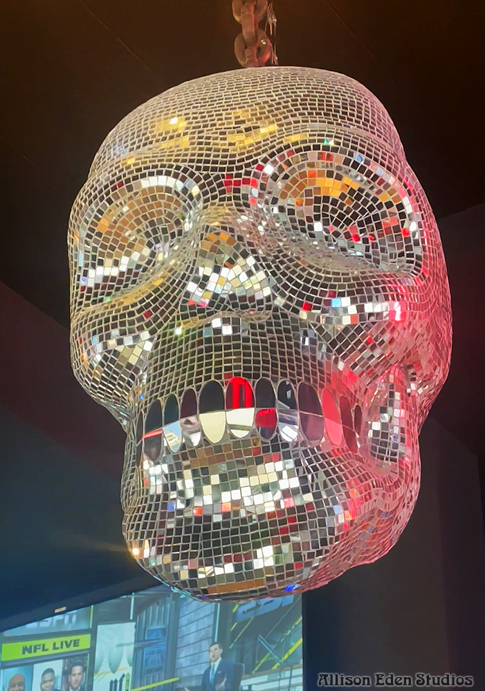 Large handcrafted mirror mosaic skull sculpture by Allison Eden Studios created for Pink Taco NYC, featuring thousands of hand-cut mirror glass tiles that reflect light like a giant disco ball hanging in restaurant.