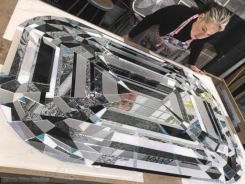 Artist Allison Eden creating a large custom glass diamond artwork from hand-cut stained glass and reflective mirror in her Brooklyn studio