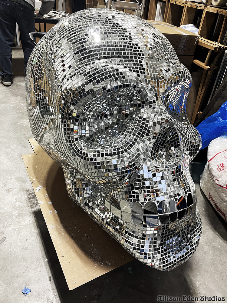 Large handcrafted mirror mosaic skull sculpture by Allison Eden Studios on dolly being created for Pink Taco NYC, featuring thousands of hand-cut mirror glass tiles that reflect light like a giant disco ball.