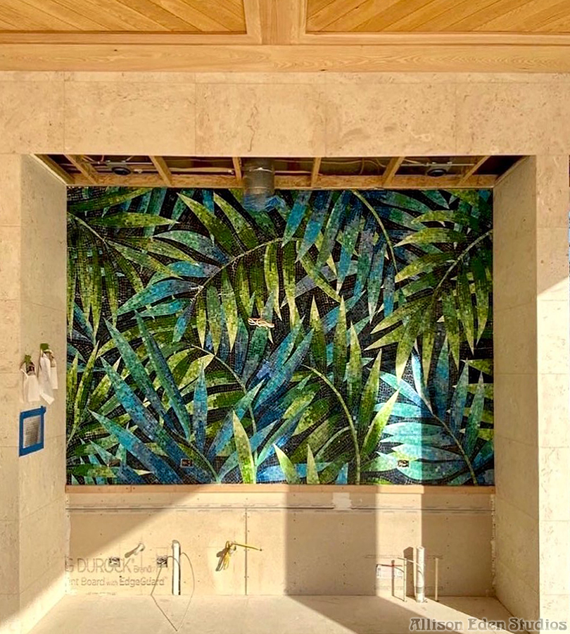 Large custom palm leaf glass mosaic backsplash being installed in a luxury outdoor kitchen