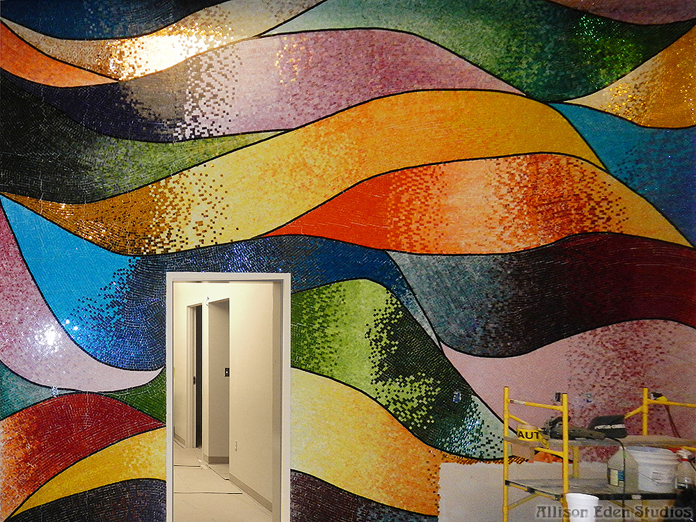 Large abstract glass mosaic wall with sweeping bands of blue, green, gold, orange, and purple