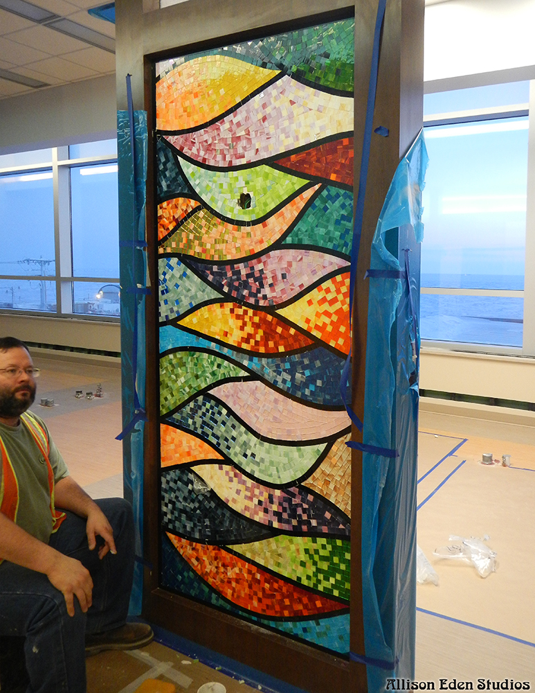 Installer beside a nearly completed stained glass mosaic panel at Samuel Simmonds Memorial Hospital