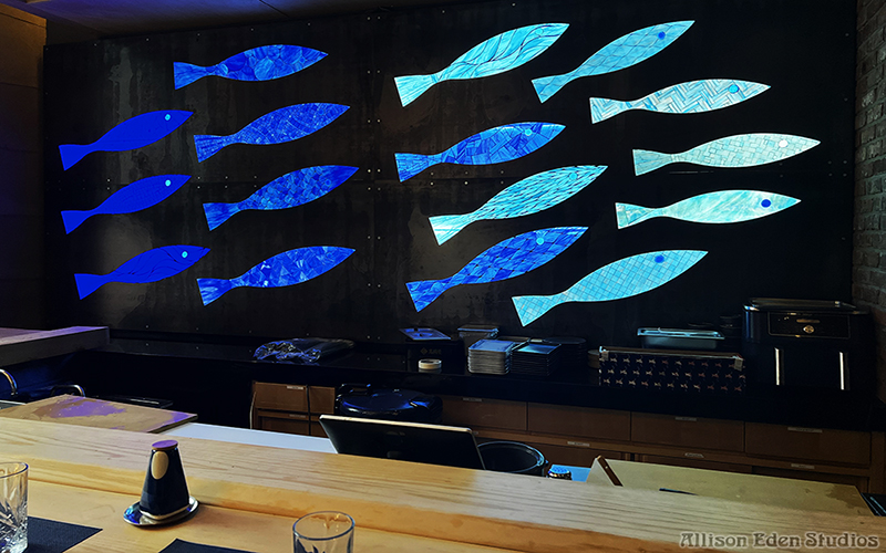 Handcrafted blue and turquoise stained glass mosaic fish illuminated from behind at Bondi Sushi in New York City.mosaic nyc small