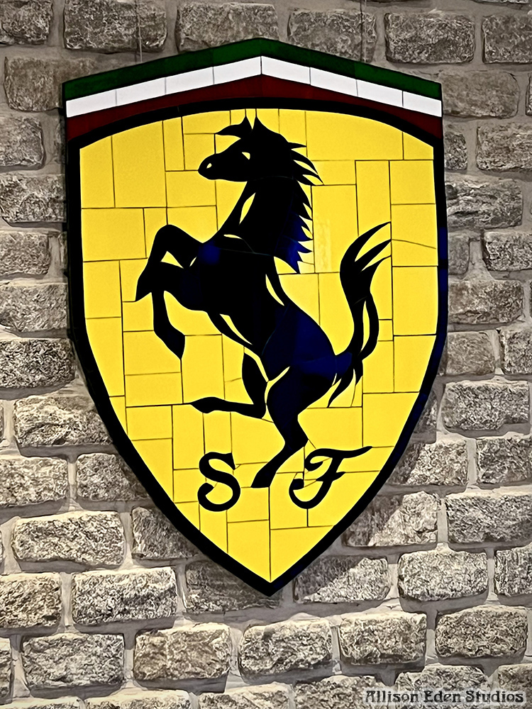 Ferrari-inspired prancing horse stained glass mosaic by Allison Eden Studios installed on a stone wall in a luxury automobile collector's space