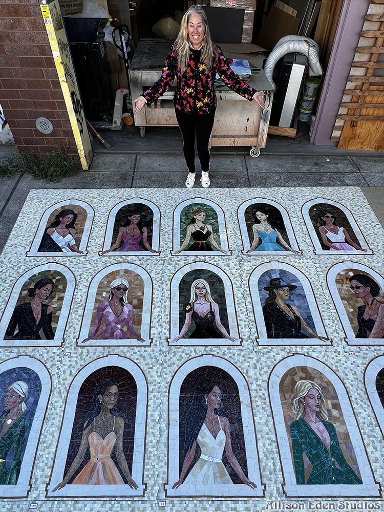 Allison Eden standing beside the large-scale Girls in Windows stained glass mosaic artwork featuring 15 handcrafted women.