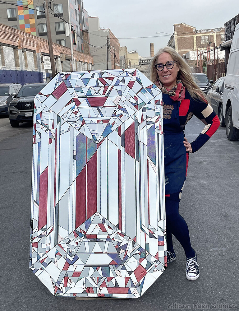 Artist Allison Eden standing beside her handcrafted Lavender Diamond stained glass and mirror mosaic artwork in Brooklyn.
