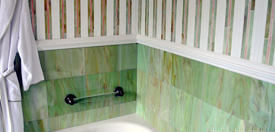 Detail of a luxury bathroom bathtub area featuring green and brown glass tile wainscoting beneath handcrafted vertical striped glass mosaic walls by Allison Eden Studios.