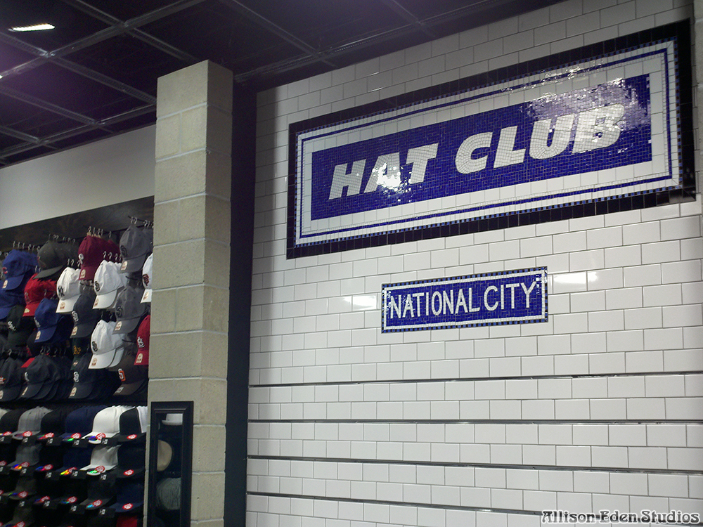 Front view of handcrafted Hat Club and National City cobalt blue and white glass mosaic retail signs installed against a white subway tile wall.