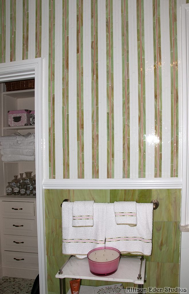 Gatsby-inspired bathroom with pastel green and pink striped glass mosaic walls, white traditional moldings, arched windows, and colorful glass vases in a Mill Neck mansion.